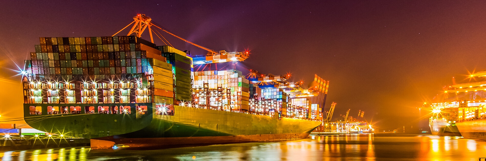 A huge international cargo ship anchored at port during a night time loading session
